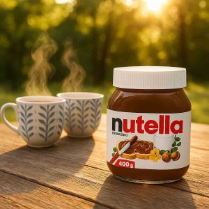 شیشه نوتلا ۴۰۰ گرمی روی میز چوبی در طبیعت همراه با دو فنجان چای داغ با بخار